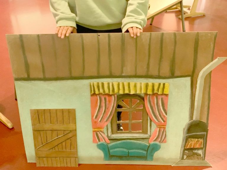 Eine gemaltes Kulissenelement mit Tür, Fenster, Couch und Kamin.