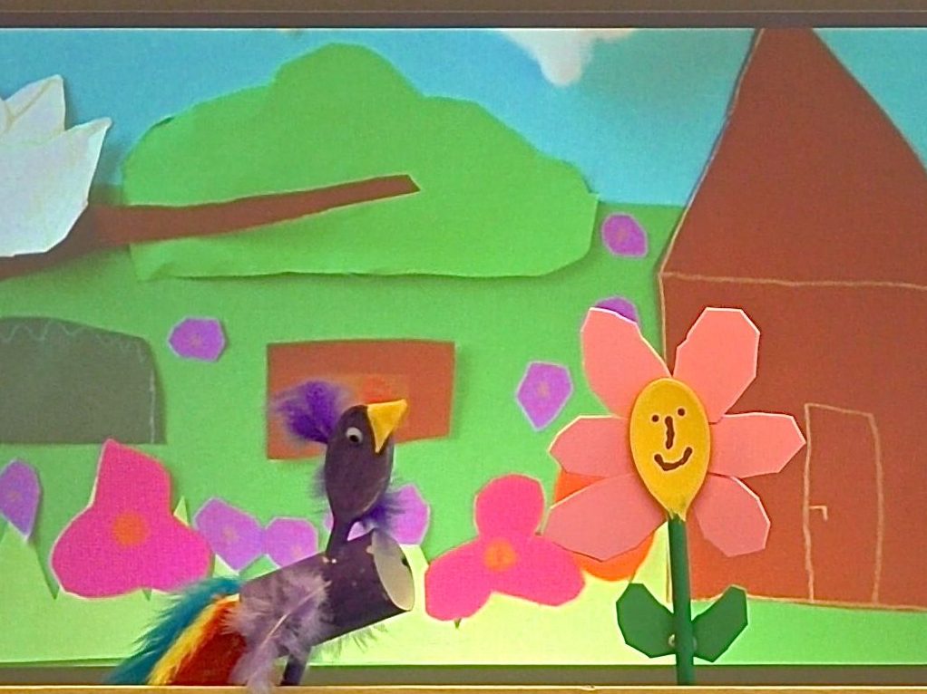 Vogel- und Blumenfigur im theakrino vor einem bunten Gartenhintergrundbild