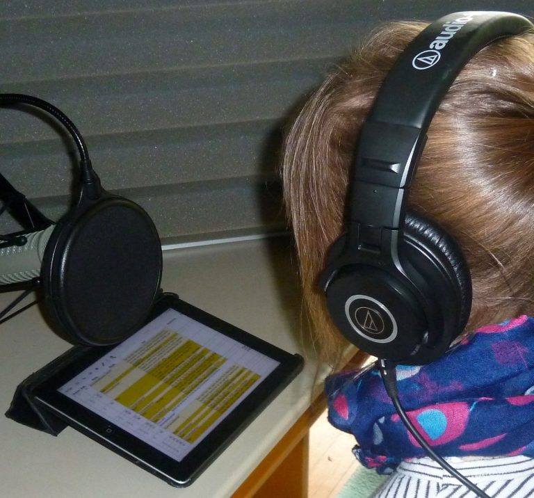 Mädchen sitzt mit Kopfhörern vor einem Tablet und Aufnahmemikrofon