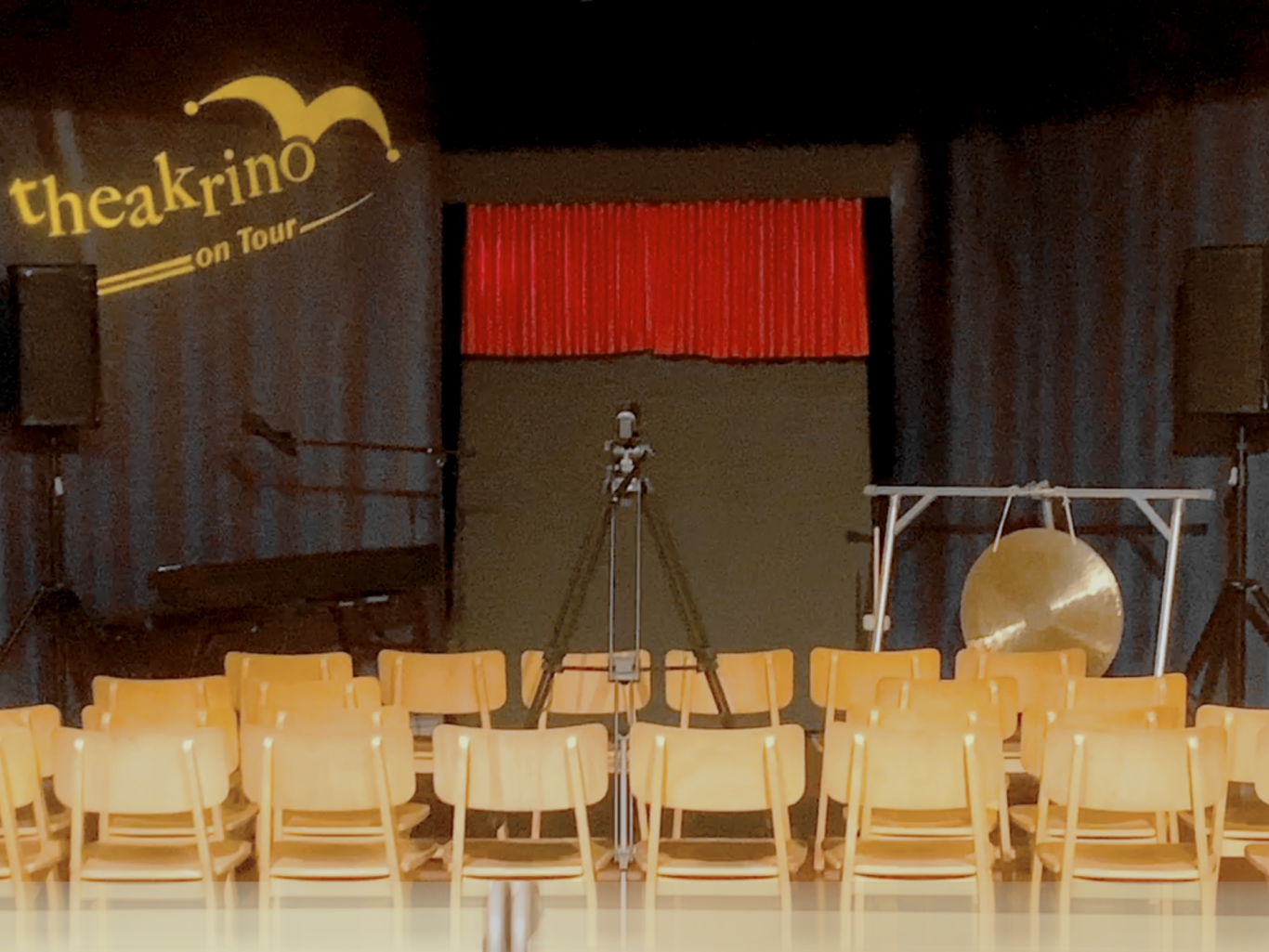 die theakrino Schul-Bühne mit rotem Vorhang vor leeren Stuhlreihen und einem Gong